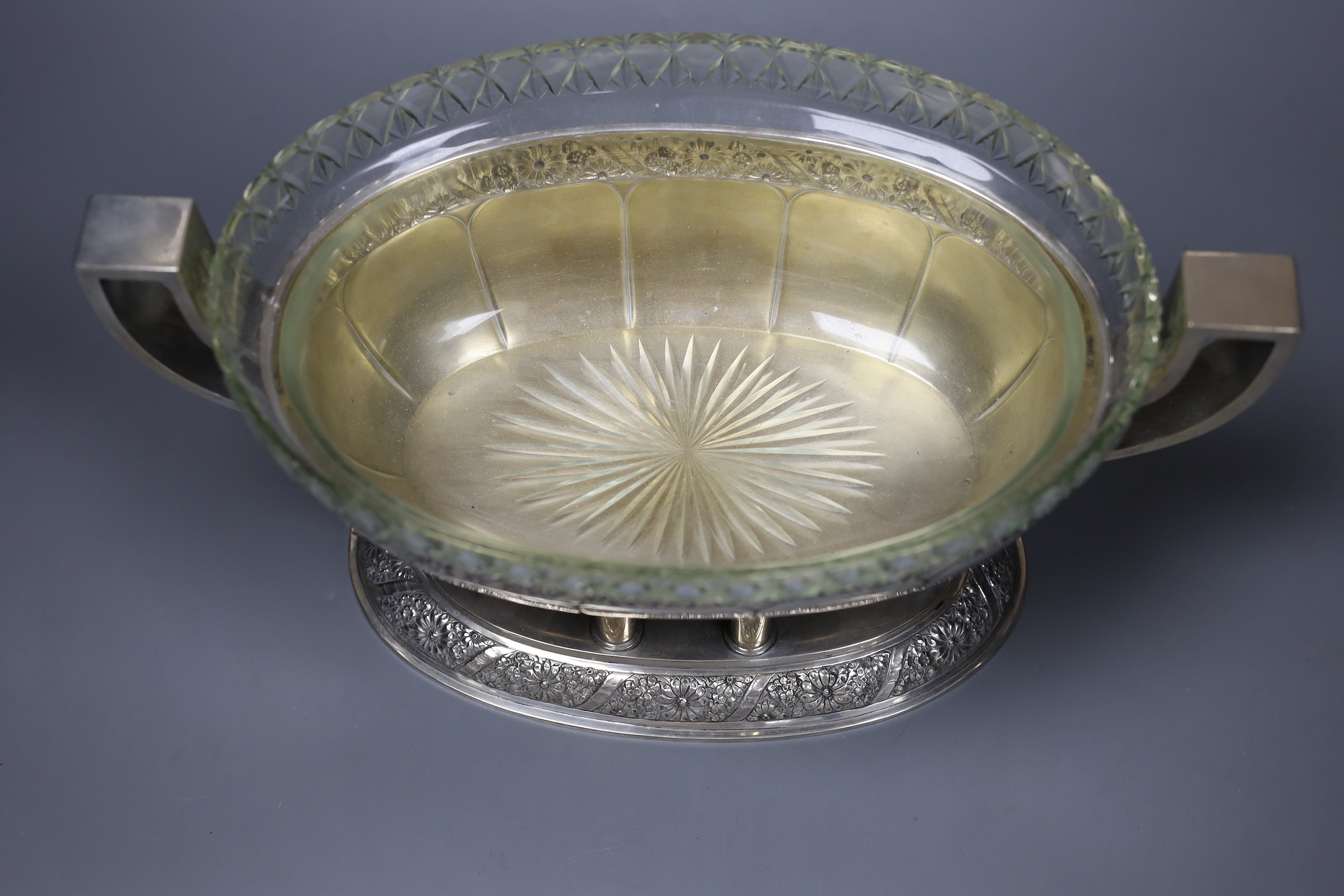 An early 20th century Continental white metal two handled centrepiece bowl, with engraved floral banded decoration and cut glass liner, 35cm over the handles.